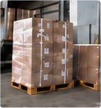 Shrink-wrapped cartons stacked on pallets at a loading dock.