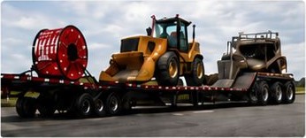 A lowboy trailer carrying a wheel loader and other heavy construction equipment.